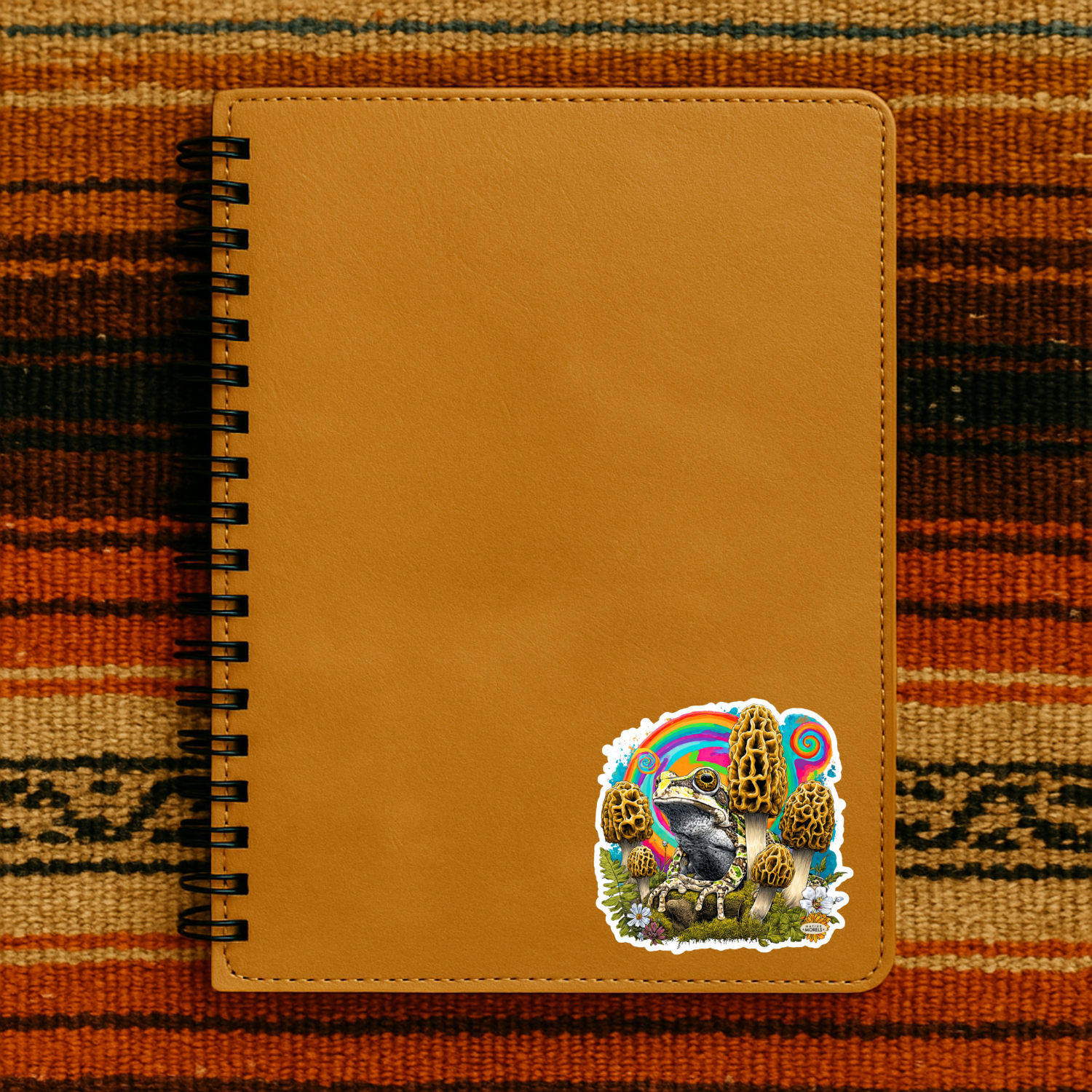 Brown notebook with a colorful sticker of a bear and rainbow on a patterned fabric background